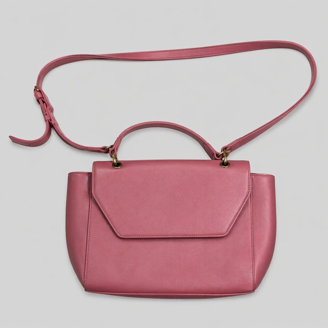 A dusty rose pink leather handbag with a top handle, a detachable shoulder strap, and a front flap, shown against a neutral light gray background.