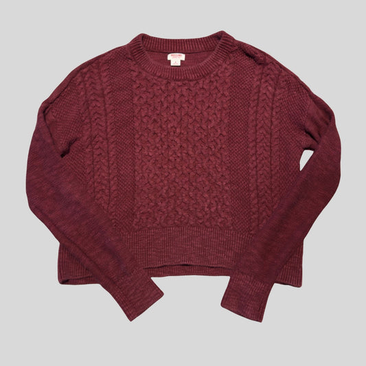 A cropped crewneck cable-knit sweater in a deep burgundy or maroon color, laid flat against a solid light gray background.