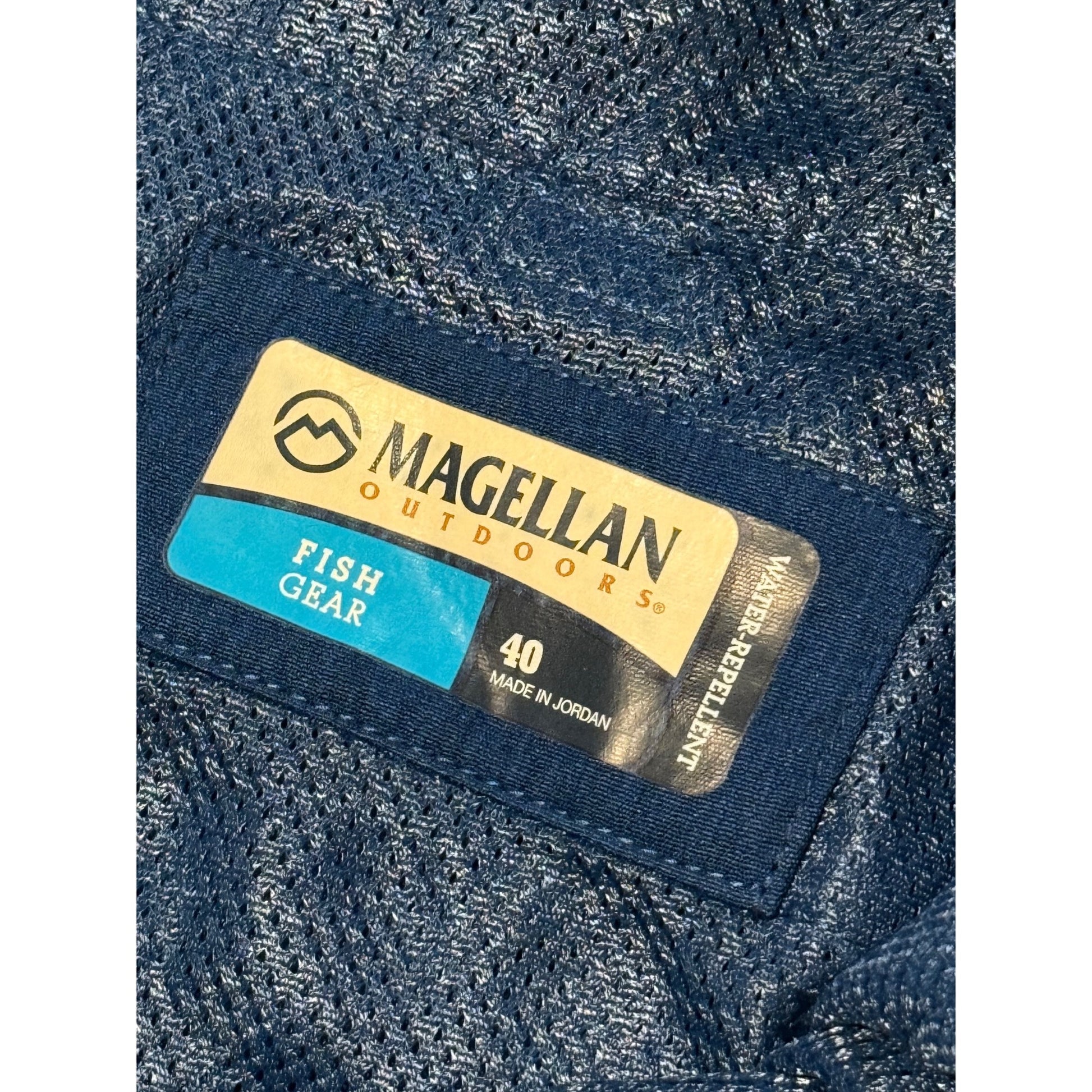 Close-up of a Magellan Outdoors Fish Gear garment label sewn onto a blue textured mesh fabric, with size 40 and Made in Jordan details visible.